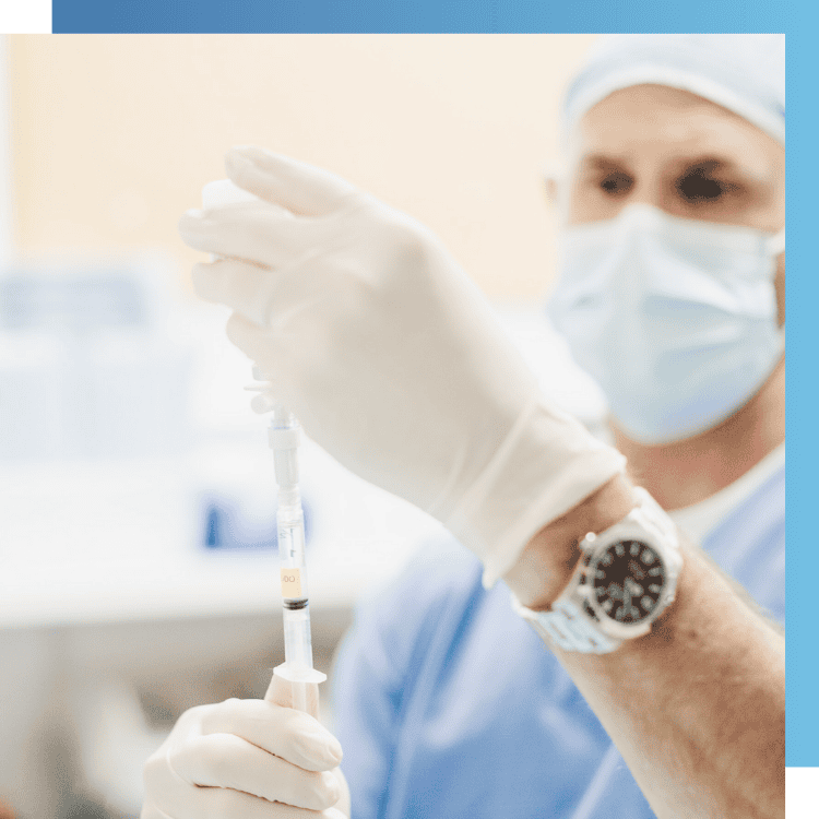 Dr. Steven Sampson wearing medical gear and a nice watch, holding a syringe